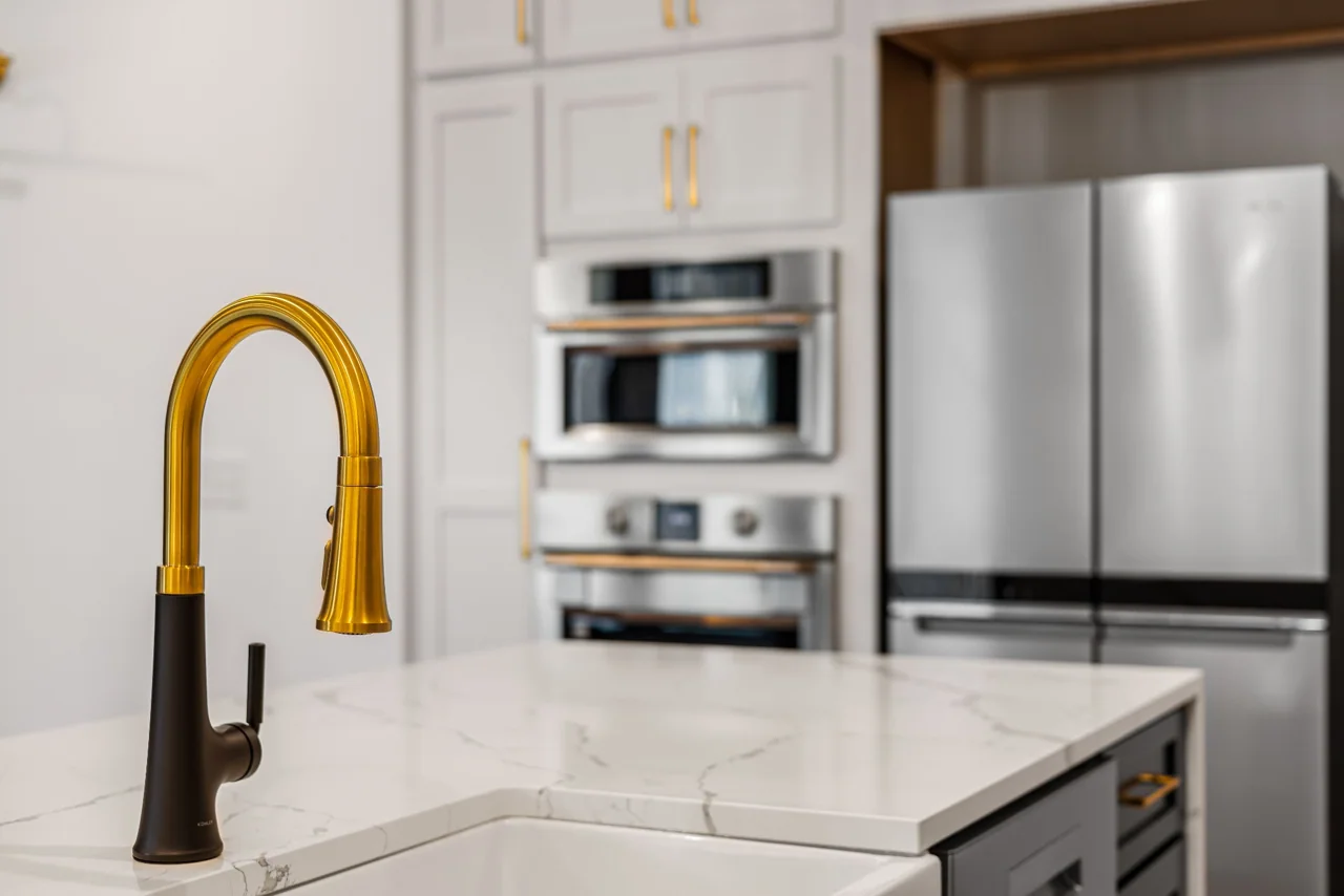 Kitchen detail with white cabinetry, pale countertop and a brass faucet