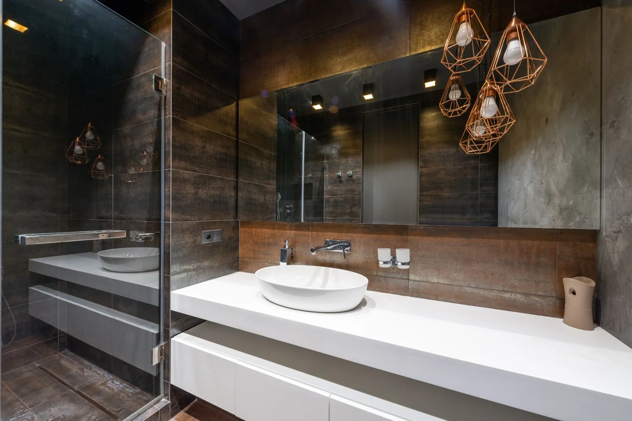 Bathroom with dark stone surfaces, white basin and warm pendant lights